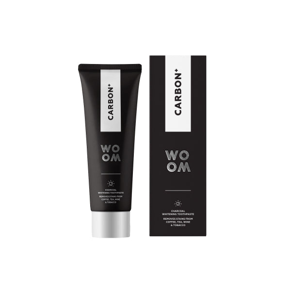 A tube of toothpaste labeled WOOM CARBON+ next to its packaging box, both featuring a black and white color scheme.