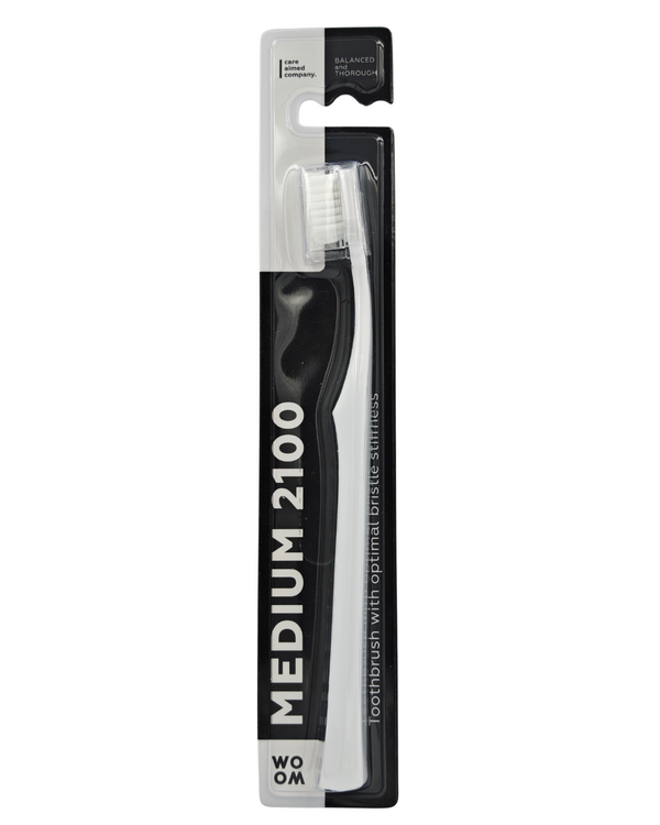 A black and white WOOM MEDIUM 2100 toothbrush in its packaging, displaying the toothbrush with white bristles and a ergonomic black handle.